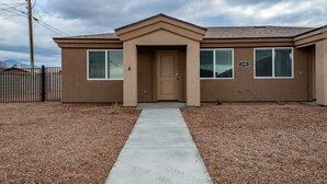 A two-story building with a beige exterior, a front door, and a number '2490' sign. - Modern Luxury Retreat | Brand-New Build | Pet-Friendly (Kingman)