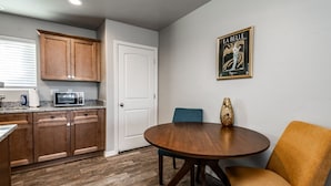 A compact kitchen with wooden cabinets, a microwave, and a dining area with a round table and two chairs. - Modern Luxury Retreat | Brand-New Build | Pet-Friendly (Kingman)