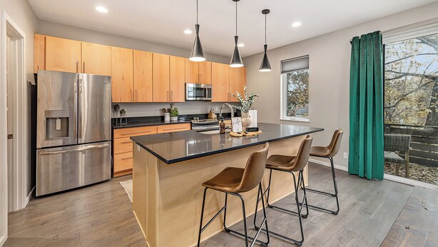 A modern kitchen with stainless steel appliances, wooden cabinets, and a central island with bar stools. -  3-bedroom townhome in Kansas City (Kansas City)