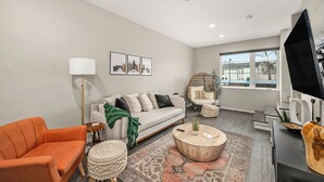 A modern living room with a sofa, armchair, and coffee table, a flat-screen TV, and a large window with a view. -  3-bedroom townhome in Kansas City (Kansas City)