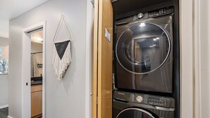 A laundry room with two stacked front-loading washers and dryers, a wooden door, and a hallway leading to a bathroom. -  3-bedroom townhome in Kansas City (Kansas City)