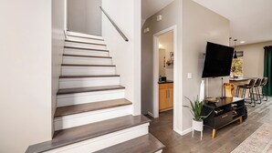 A staircase with wooden steps and a handrail, leading to a dining area with a TV and a plant. -  3-bedroom townhome in Kansas City (Kansas City)