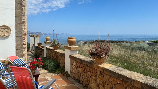 A terrace with a stone wall, potted plants, and striped lounge chairs overlooking a coastal view. - 3 bedroom nice home in Colonia de Sant Pere (Colonia de Sant Pere)
