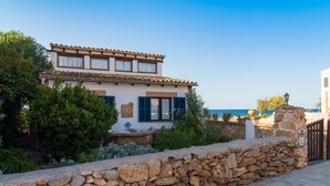 A two-story building with a stone wall in front, a tiled roof, and a view of the sea. - 3 bedroom nice home in Colonia de Sant Pere (Colonia de Sant Pere)