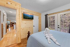 Ein Schlafzimmer mit Holzpaneelen an der Wand, einem Bett mit weißer Decke und einem darüber montierten Fernseher.