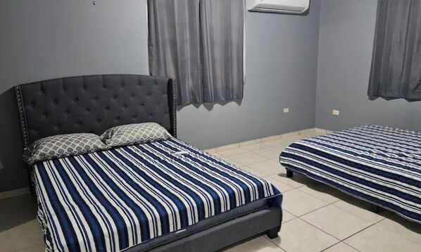 Une chambre à coucher avec un lit doté d’une tête de lit capitonnée, une literie à rayures et une petite table de chevet.