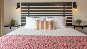 Una cama con una colcha blanca y roja estampada, un cabecero de madera y dos mesitas de noche con lámparas.