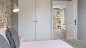 Une chambre à coucher comprenant un lit, une table de chevet, une lampe, une armoire et donnant sur un balcon.