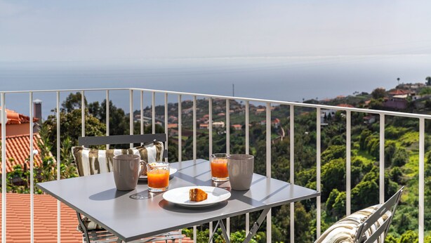 Un balcon avec une table préparée pour le petit-déjeuner, offrant une vue sur un paysage côtier.