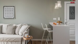 Un salon moderne avec un canapé, une petite table ronde sur laquelle se trouvent une tasse et une assiette, et un coin cuisine avec un comptoir et des chaises.