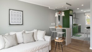 Un salon moderne avec un canapé blanc, un coin repas doté d’un petit îlot, et une cuisine avec des meubles verts.