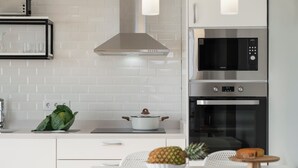 Eine moderne Küche mit weißen Schränken, einer Edelstahl-Dunstabzugshaube, einer Mikrowelle und einem Backofen. Auf der Arbeitsplatte steht eine Obstschale und ein weißer Tisch mit Stühlen.