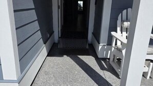 A covered porch with a black mat leading to a door, white chairs, and a clear view into the house. - Panama City Beach 4BR | Private Heated Pool (Panama City Beach)