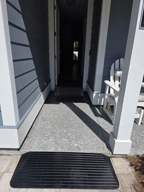 A covered porch with a black mat leading to a door, white chairs, and a clear view into the house. - Panama City Beach 4BR | Private Heated Pool (Panama City Beach)