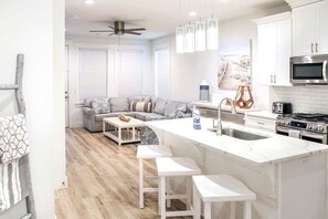 A modern kitchen with white cabinetry, a central island with bar stools, a microwave, stove, and a large window with blinds. - 4-Bedroom Panama City Beach Home with Private Heated Pool (Panama City Beach)