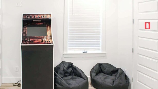 A room with a gaming console, two bean bags, a window with blinds, and a white door with a red emergency exit sign. - Panama City Beach 4BR | Private Heated Pool (Panama City Beach)