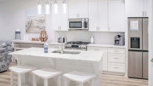 A modern kitchen with white cabinetry, a central island with stools, stainless steel appliances, and pendant lighting. - Panama City Beach 4BR | Private Heated Pool (Panama City Beach)