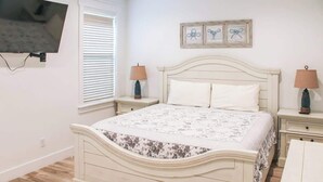 A bedroom with a bed, two bedside tables, a TV mounted on the wall, and a window with blinds. - Panama City Beach 4BR | Private Heated Pool (Panama City Beach)