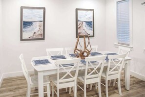 A dining area with a white table and chairs, framed artwork on the walls, and a window with blinds. - 4-Bedroom Panama City Beach Home with Private Heated Pool (Panama City Beach)