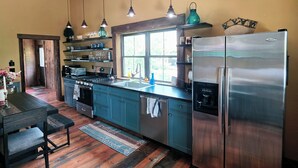 Uma cozinha moderna com armários cor turquesa, uma geladeira de aço inoxidável e luminárias pendentes.