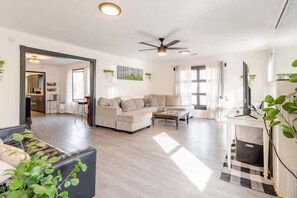 Amplia sala de estar con sofá, mesa de centro y televisor, un comedor y una cocina al fondo.