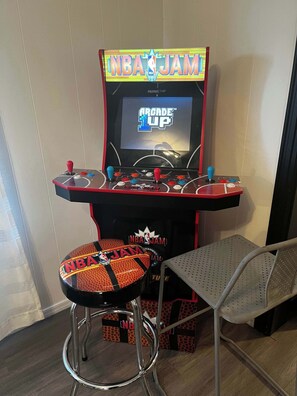 An arcade machine with NBA JAM branding, a stool, and a metal chair. - Brews, Pines, & Peaks | Your downtown Flagstaff stay awaits. (Flagstaff)