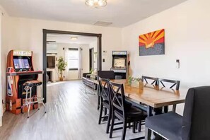 Un área de comedor con una mesa y sillas de madera, máquinas de videojuegos y una pared con un cartel.