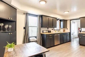 A modern kitchen with dark cabinetry, a wooden dining table, and a small potted plant. - Brews, Pines, & Peaks | Your downtown Flagstaff stay awaits. (Flagstaff)