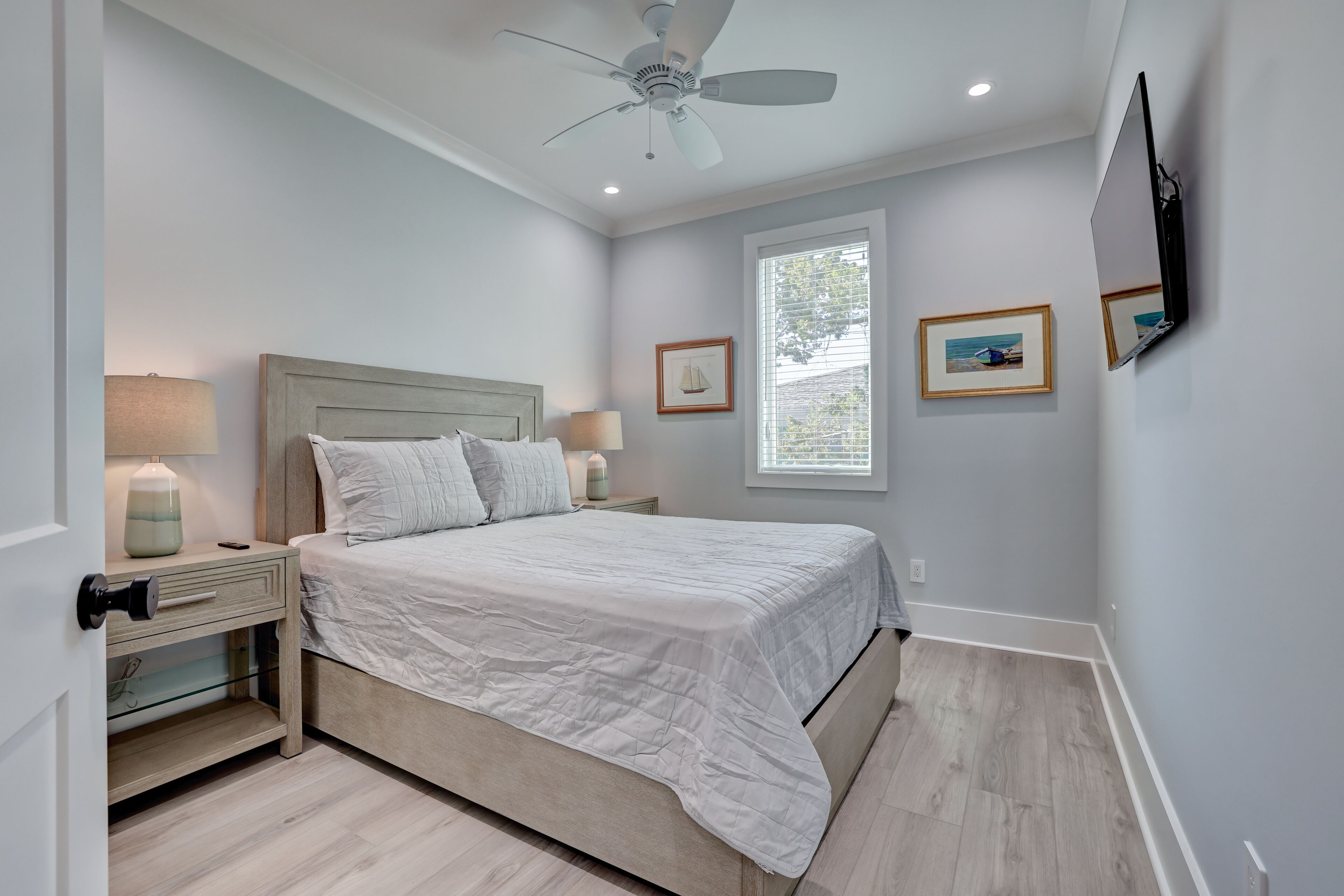 A bedroom with a bed, nightstands, a ceiling fan, and framed pictures on the wall.