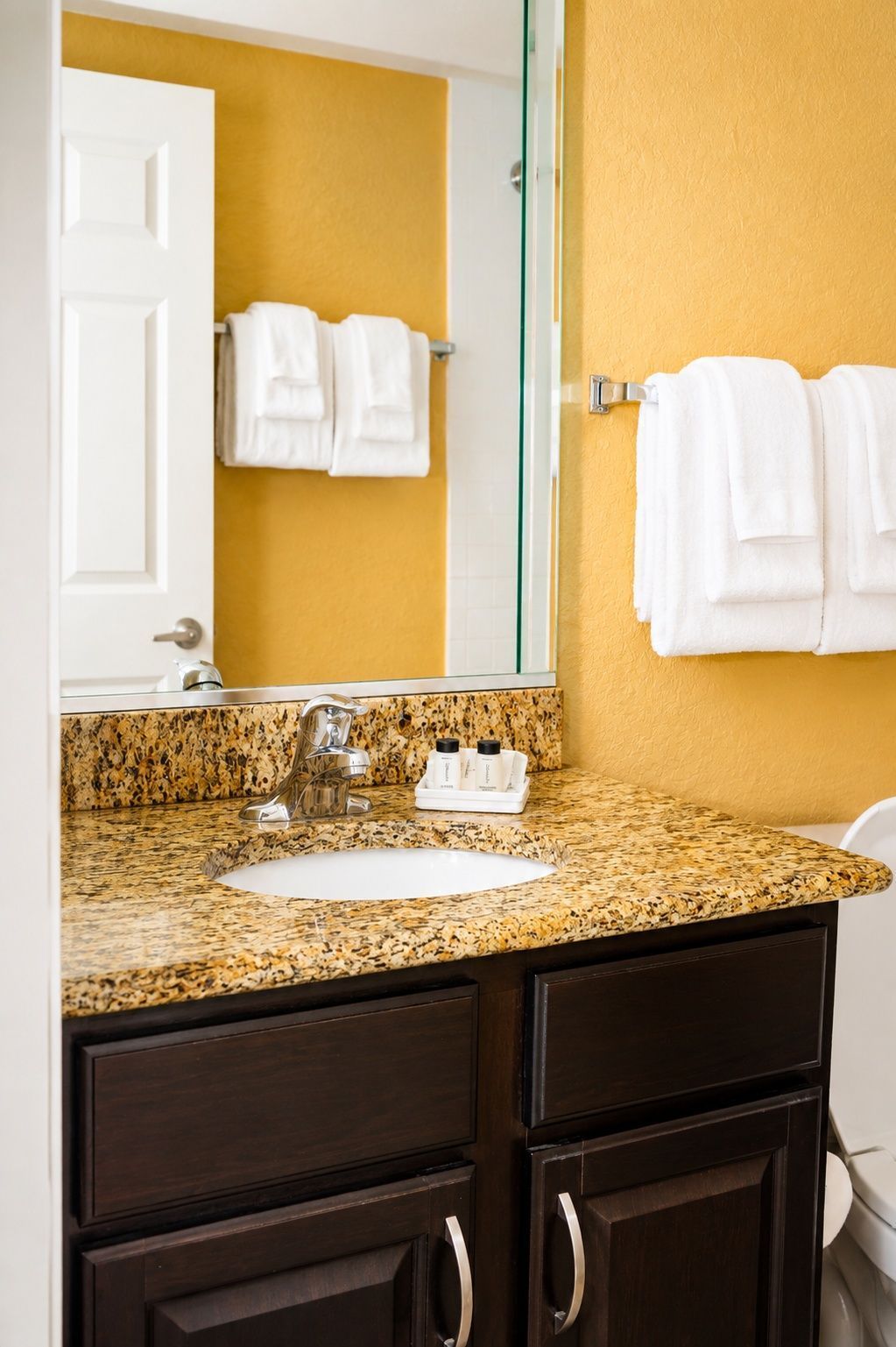 A bathroom with a granite countertop, a sink, a mirror, and a towel rack with white towels.