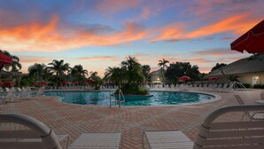 A pool area with lounge chairs and umbrellas, surrounded by palm trees and buildings. - 1BR Condo w/ Kitchen + Resort Perks | Near Disney! (Kissimmee)