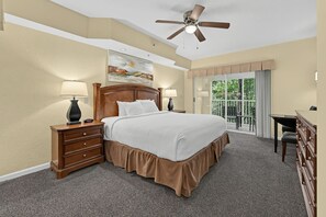 Ein Hotelzimmer mit einem großen Bett, einem Schreibtisch, einem Sessel, einem Deckenventilator und einem Bild an der Wand.