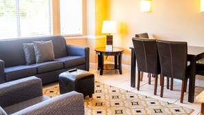 A modern living room with a sofa, ottoman, and patterned rug. There is a dining area with chairs and a table, and a lamp on a side table. - Near Disney! 1BR Deluxe Condo w/ Full Kitchen (Kissimmee)