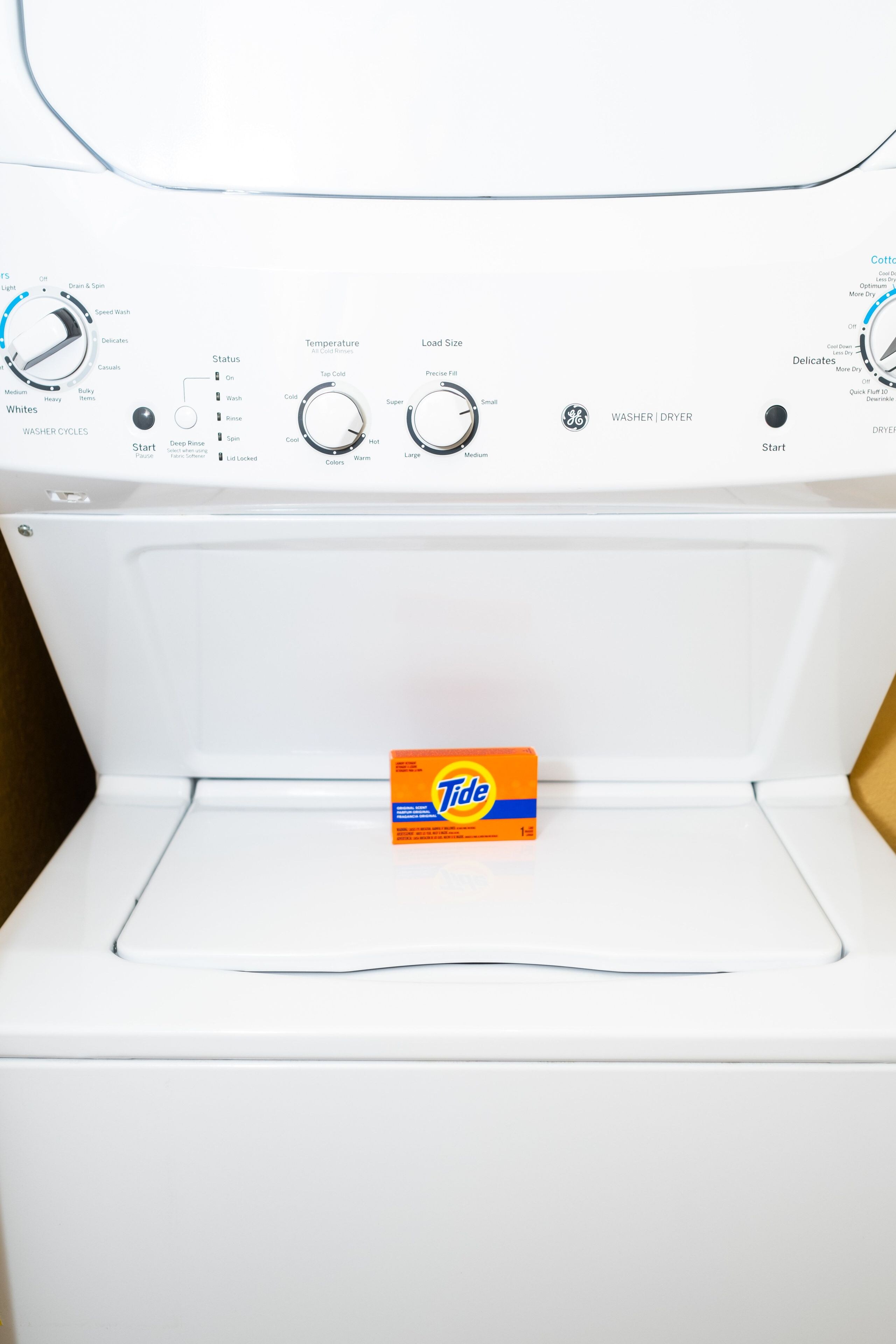A front view of a white washing machine with Tide detergent box inside.