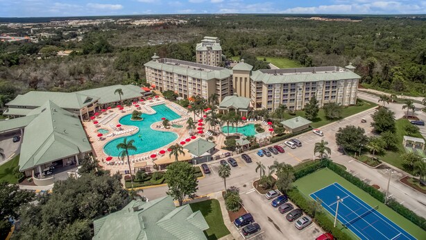 A large hotel with a central swimming pool, multiple guest rooms, and a tennis court. - Near Disney! 1BR Deluxe Condo w/ Full Kitchen (Kissimmee)