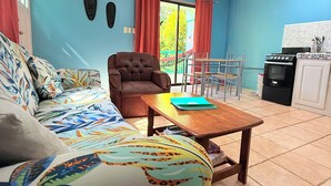 A living room with a sofa, armchair, and a dining table. There is a kitchen area with a stove and cabinets. - #2 Cozy 1-bedroom apartment in Cahuita w/ AC, parking-near beach, national park (Cahuita)