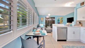 Una cocina moderna con gabinetes blancos, lavavajillas integrado y un comedor con mesa y sillas.