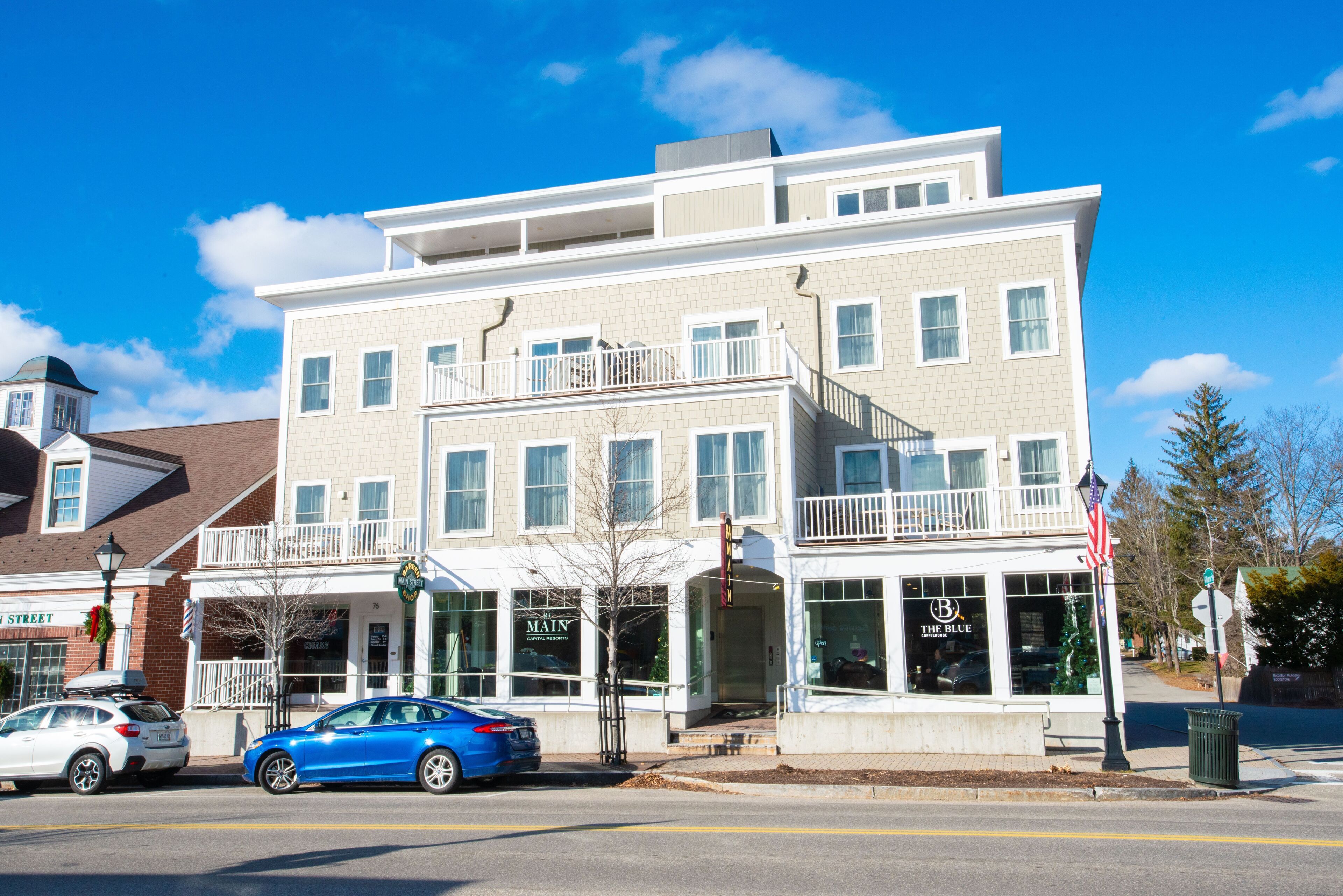 A multi-story building with a ground-level storefront, a balcony on the second floor, and a visible American flag.