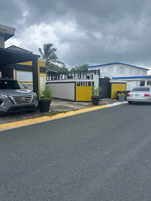 Une entrée fermée par un portail mène à une propriété appelée « Villa Lago », devant laquelle est garée une voiture grise.