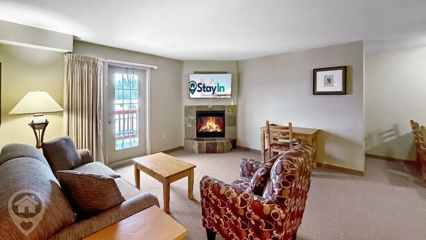 Ein Wohnzimmer mit einer Couch, einem Sessel, einem Couchtisch, einem Kamin, einem Fernseher und einem Essbereich mit Stühlen.