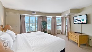 Ein Hotelzimmer mit einem großen Bett, einem Fernseher, einer Holzkommode und einem Fenster mit Vorhängen.