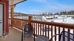 Ein Balkon mit Holzgeländern mit Blick auf einen verschneiten Parkplatz und eine Berglandschaft.