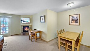 Ein Wohnzimmer mit Kamin, einem Esstisch mit Stühlen, einem an der Wand montierten Fernseher und einem gerahmten Bild.