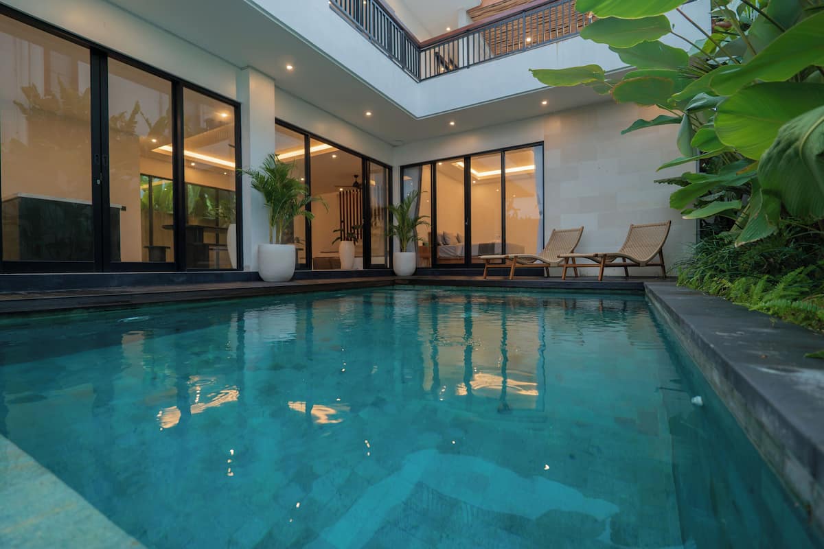 Piscina com parede de vidro, espreguiçadeiras e plantas em vasos.