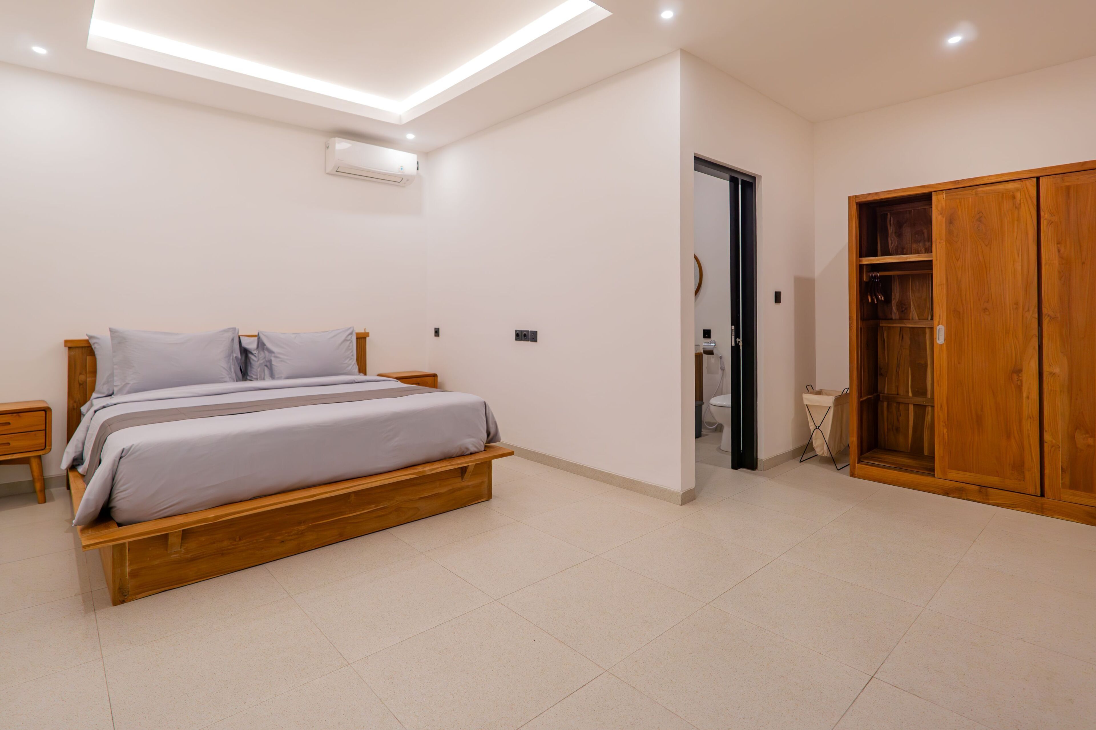 Une chambre à coucher avec un lit en bois, une armoire et une salle de bain visible à travers une porte ouverte.
