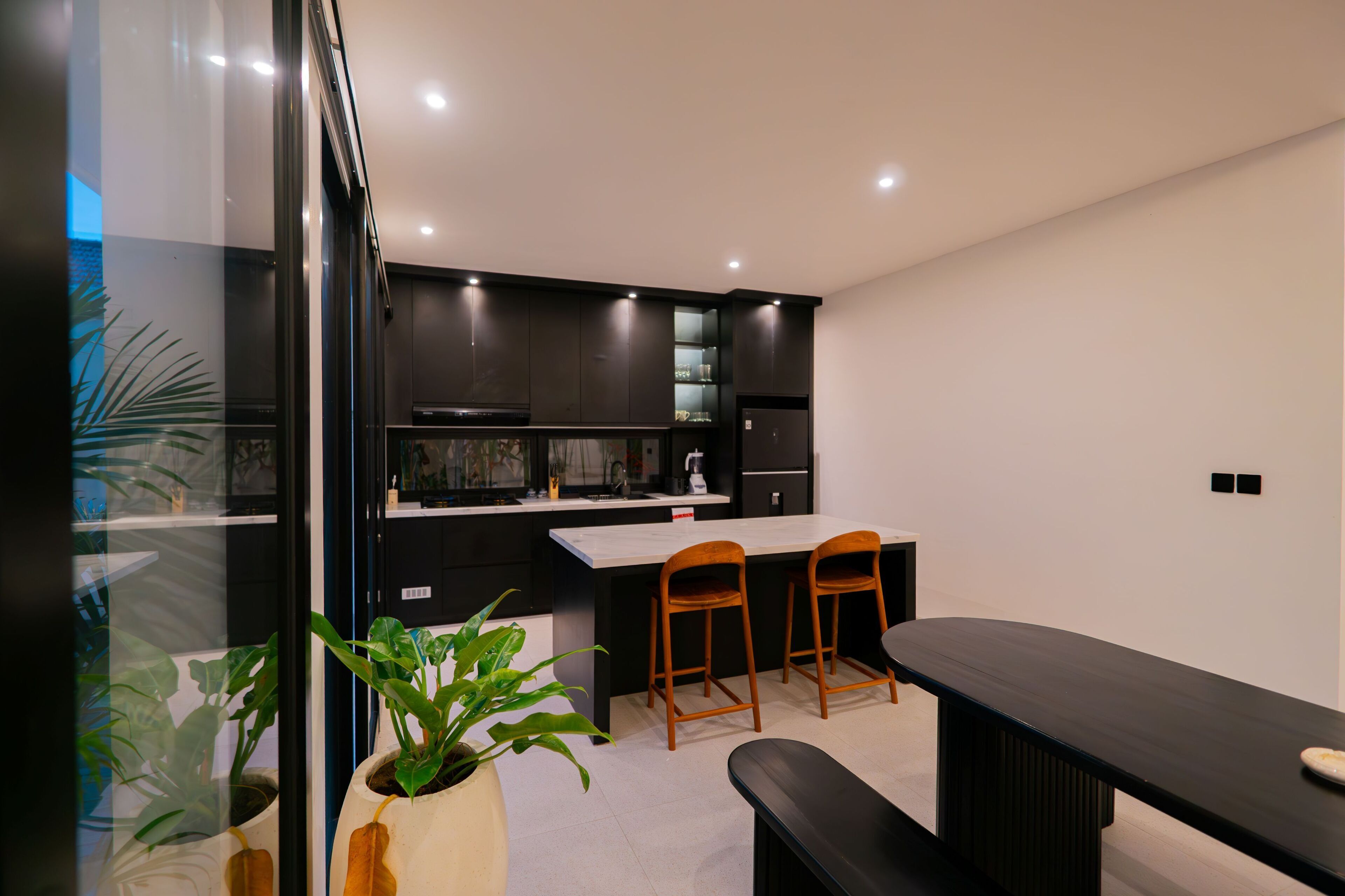 A modern kitchen with dark cabinetry, a white countertop, and two wooden bar stools.