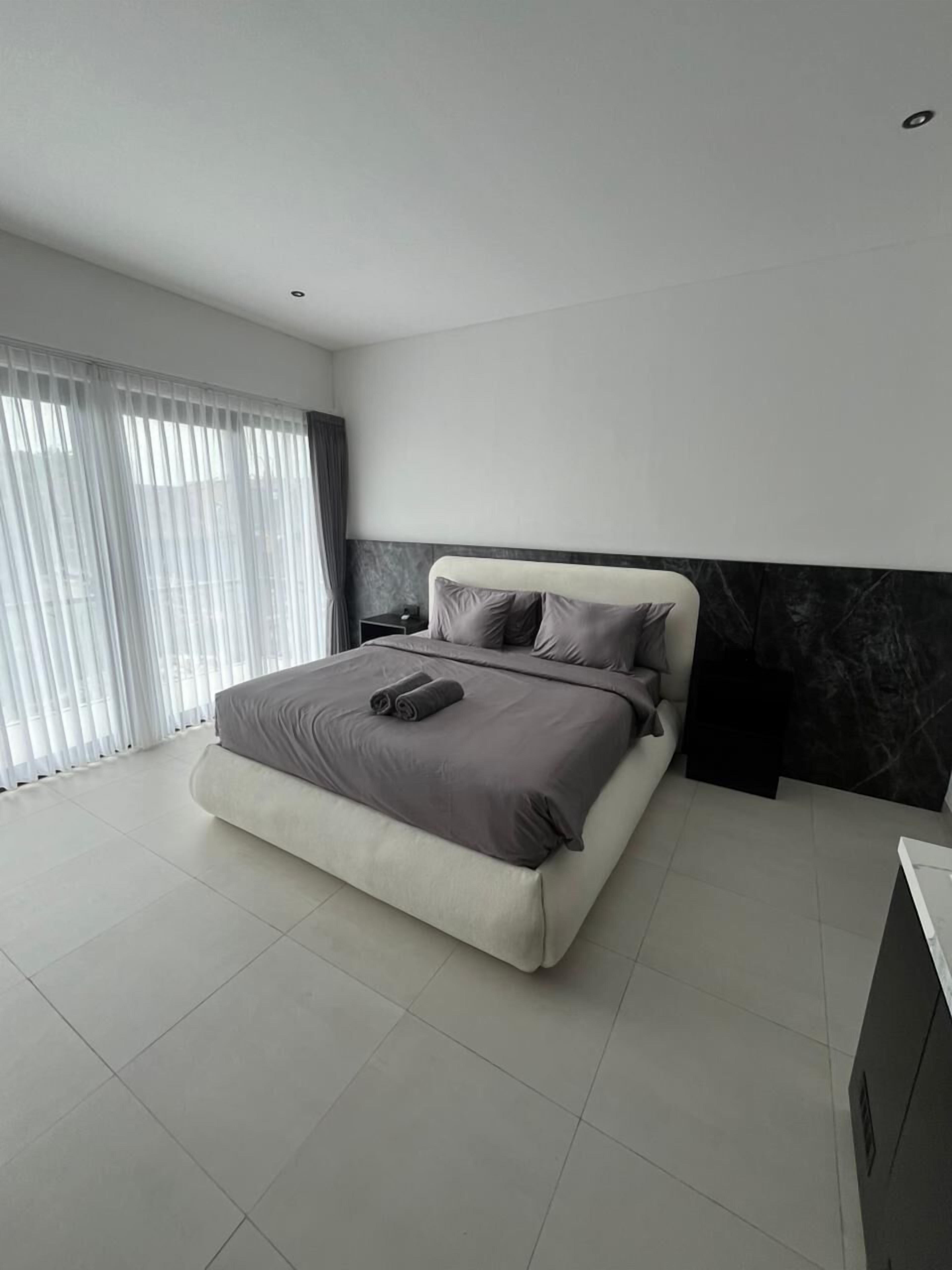 A modern bedroom with a large bed, a nightstand, and a marble accent wall.