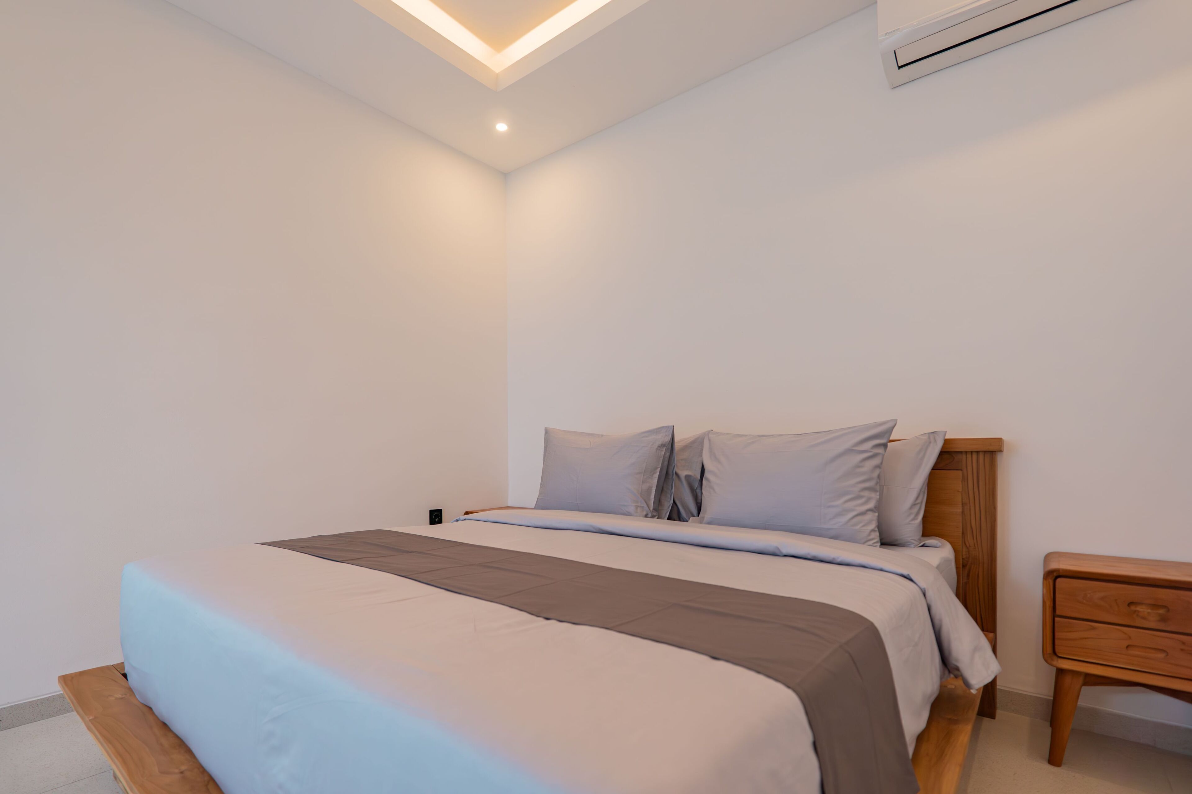 Un dormitorio con cama, mesita de noche de madera y lámpara en el techo.