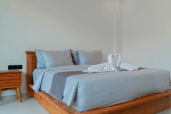 A neatly made bed with a wooden headboard, a small wooden nightstand with drawers, and a white towel folded on the bed. - Pasih Seseh Villa and Apartment by Bali Cabin (Munggu)