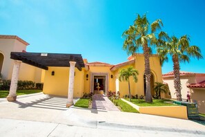 A yellow building with a covered entrance, palm trees, and a clear blue sky. - PB Montecristo 4 Mother's Day 3BR/3.5BA Striking Ocean View Private Pool/Hot Tub (Cabo San Lucas)